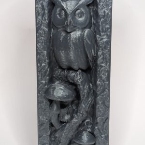 Dark gray relief sculpture depicting an owl perched above mushrooms and a skull in a vertical rectangular frame