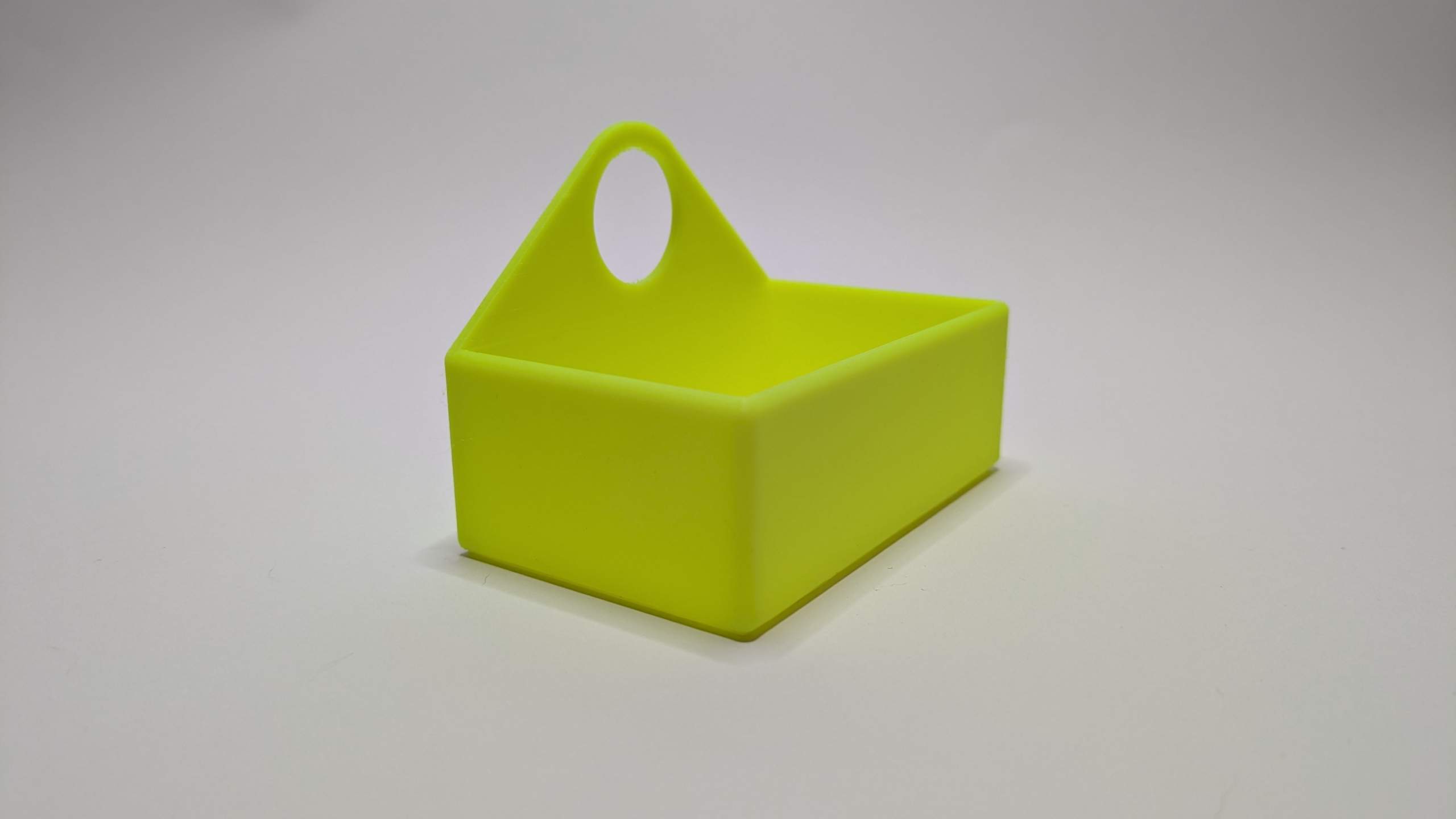 Tape Measure Holder3 Bright yellow-green plastic tape measure holder with oval handle cutout and rectangular storage compartment